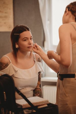 A makeup artist applying cosmetics in a softly lit room with professional equipment.