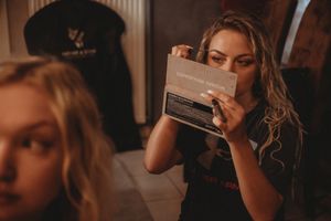 A stylist holding up a makeup tool in warm atmospheric lighting during wedding preparations.