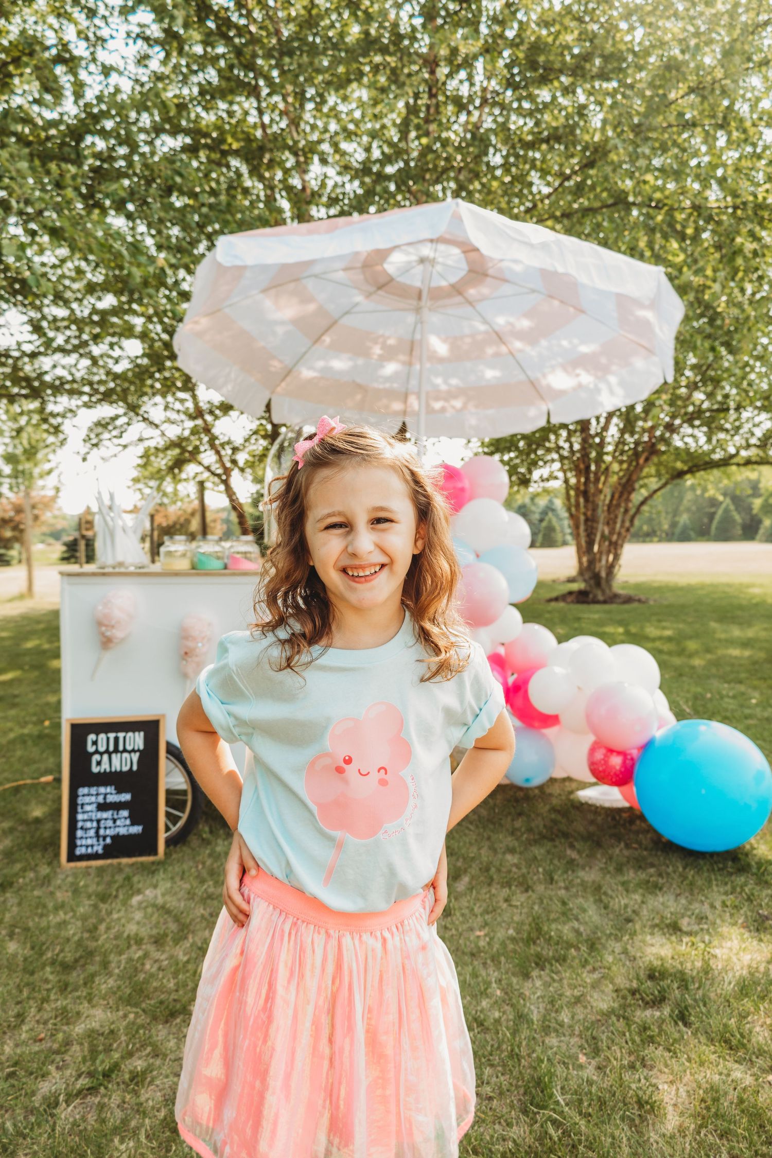 Whimsical garden party scene with parasols, balloons, and cotton candy station at sunset.