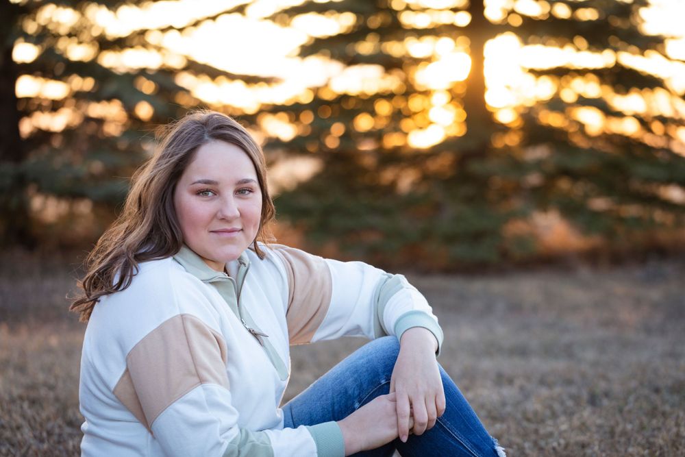 A casual portrait at sunset with evergreen trees silhouetted in the background.