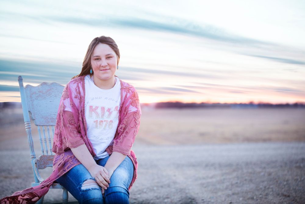Outdoor portrait at sunset with someone sitting on a chair wearing a pink cardigan and jeans.