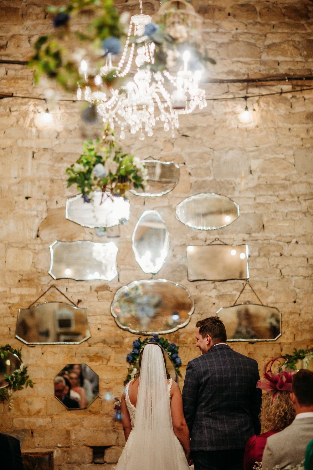 Elegant wedding venue decorated with vintage mirrors and crystal chandelier against stone wall.