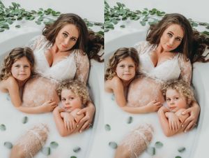 Maternity milk bath with two toddlers with leaves, surrounded by greenery.