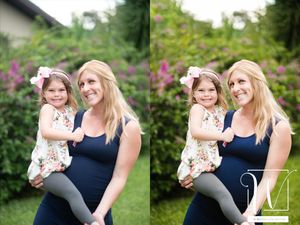 A woman in a blue dress holding a toddler in a floral outfit, both standing in a garden.