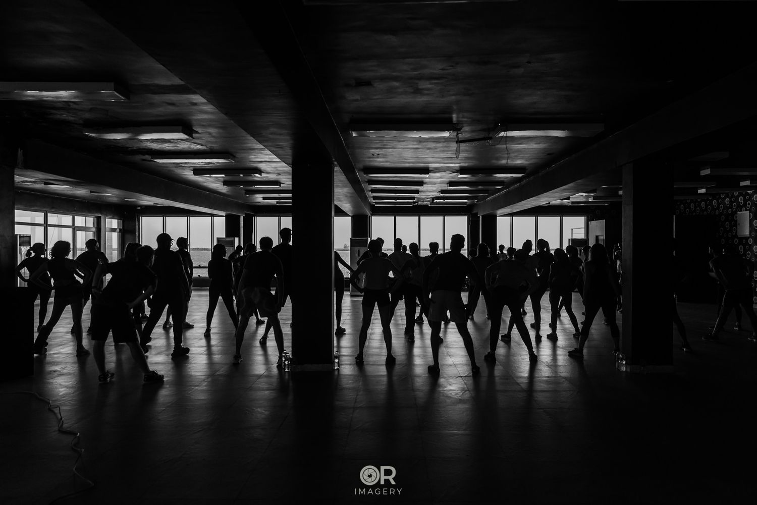 Silhouettes of dancers in a dark room with bright windows behind them.