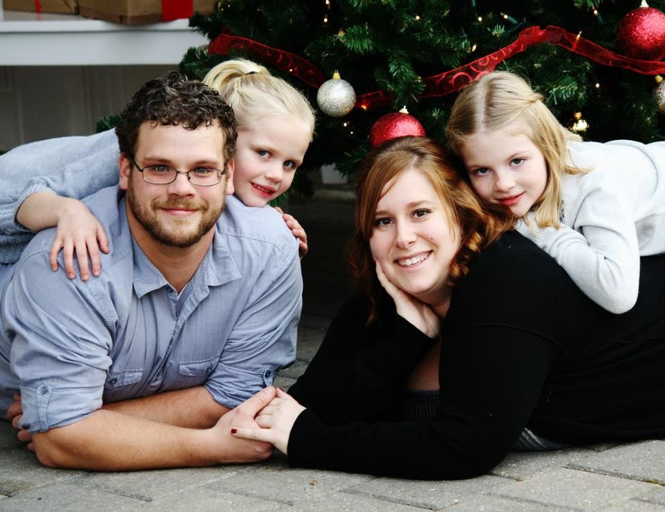 Family holiday portrait with Christmas tree and decorations in the background.