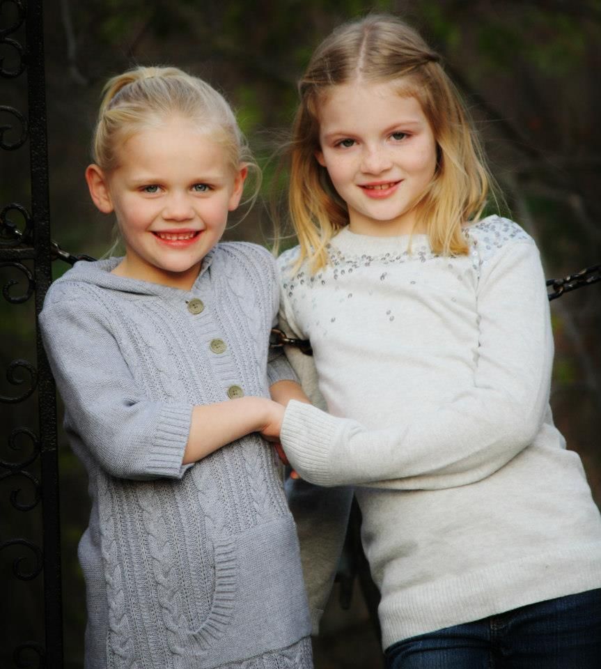 Two children in cozy winter sweaters embrace while posing for a photo.