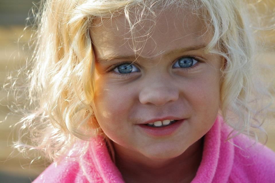 Close-up portraits of a young child with blonde hair wearing pink in natural sunlight.