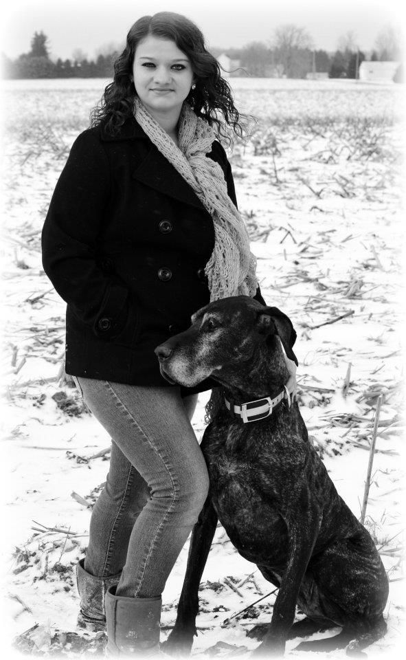 Winter scene with someone posing alongside a large black dog in the snow.