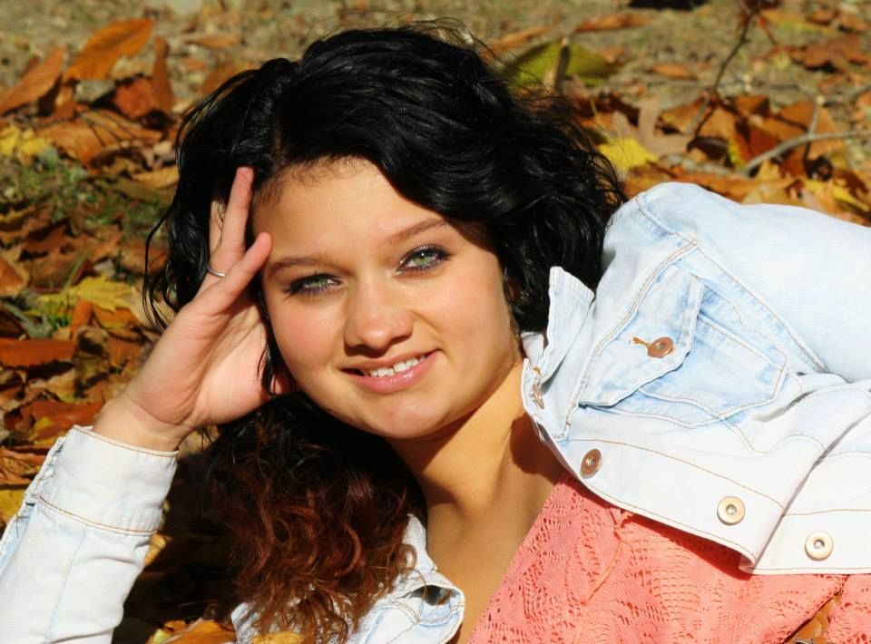 Portrait of someone with curly dark hair wearing a denim jacket in autumn leaves.