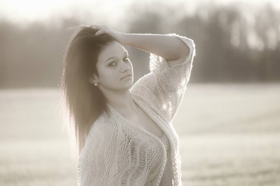 A dreamy outdoor portrait in soft light with a white knit sweater and long dark hair.