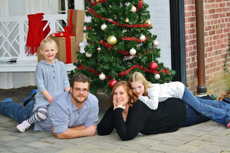 Family photo session with decorated Christmas tree and brick wall background.