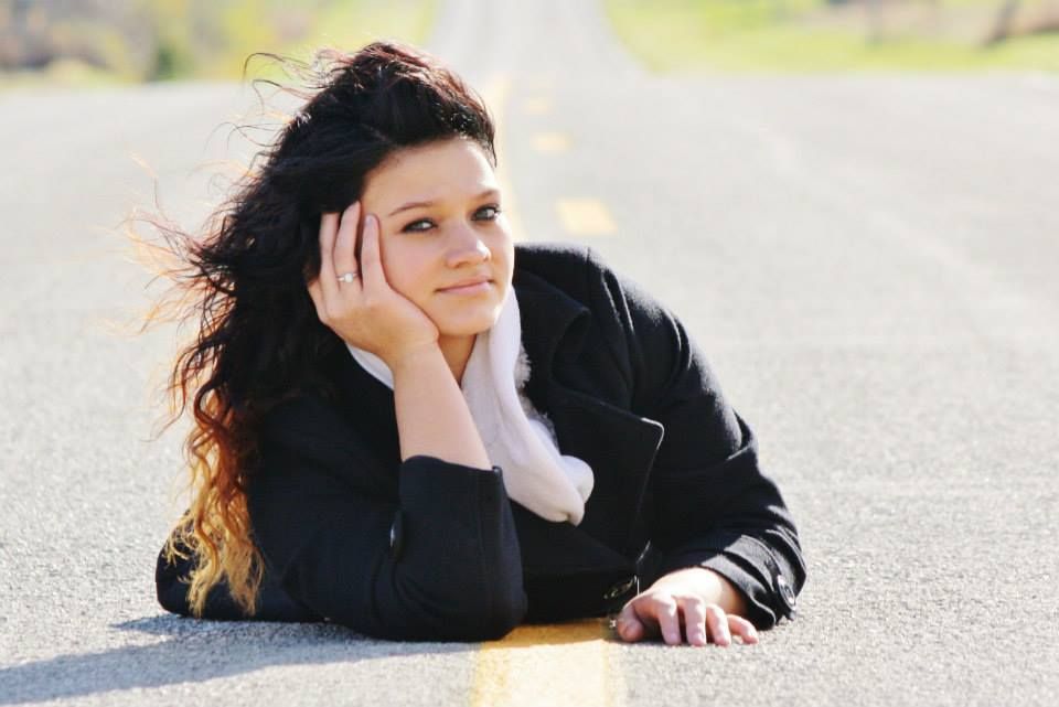 A person in black clothing lies on pavement during an outdoor photo session.