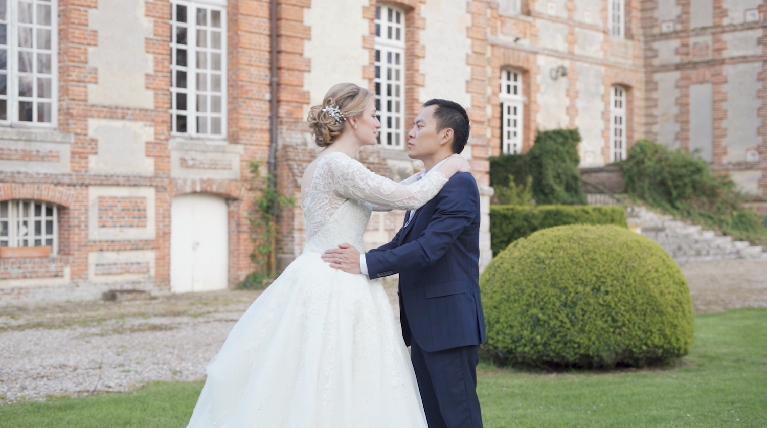 Wedding couple shares romantic moments in front of historic brick building with manicured gardens.