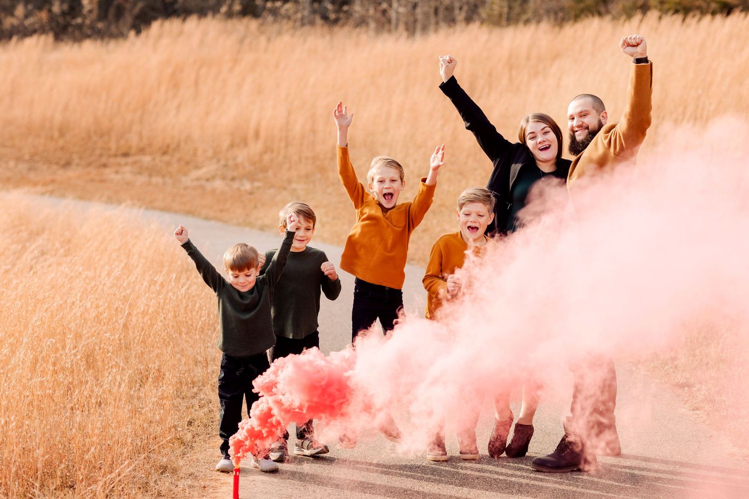 Friends celebrate with colorful smoke bombs in tall golden grass field.