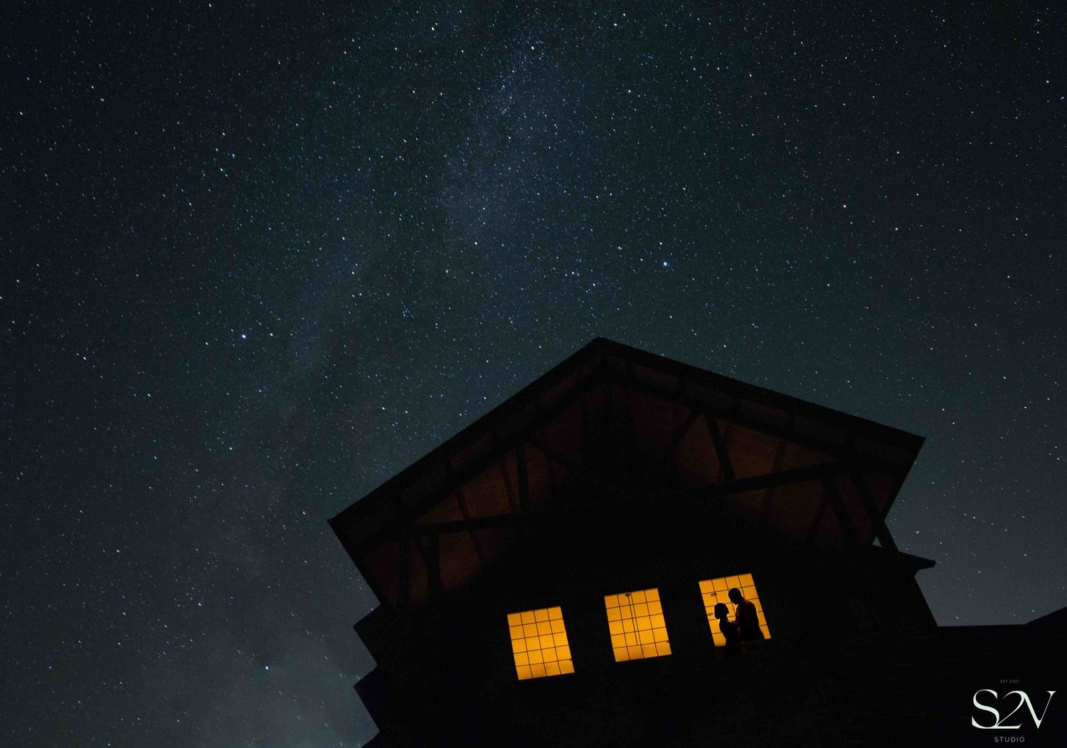 A cabin with illuminated windows glows against a starry night sky.