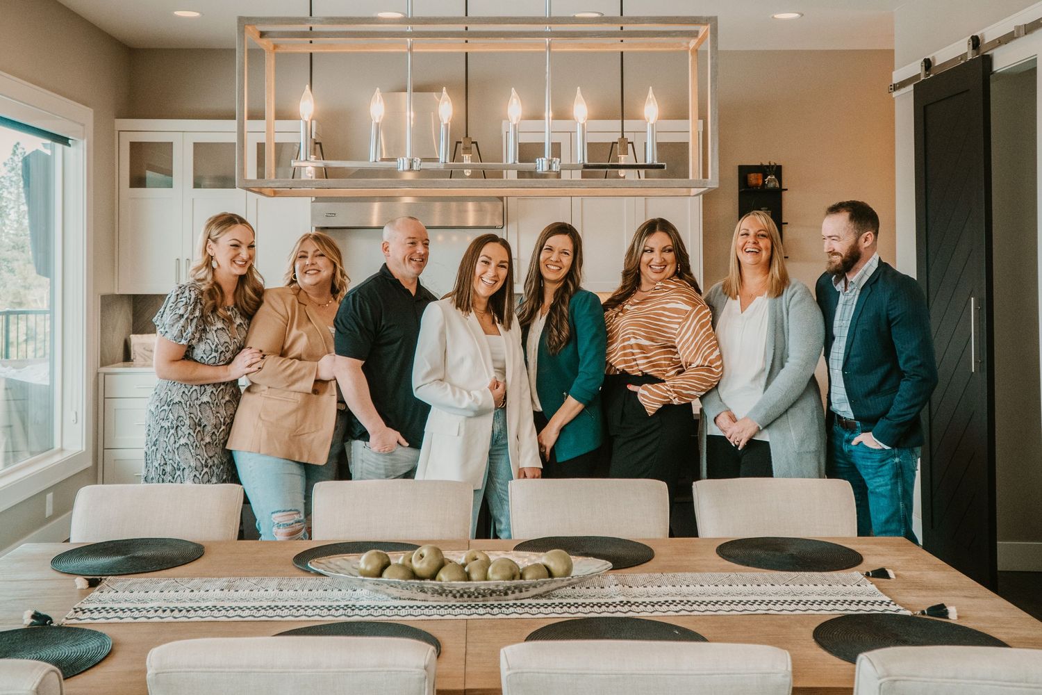 Group photo of people gathered around a modern dining table with elegant chandelier overhead.
