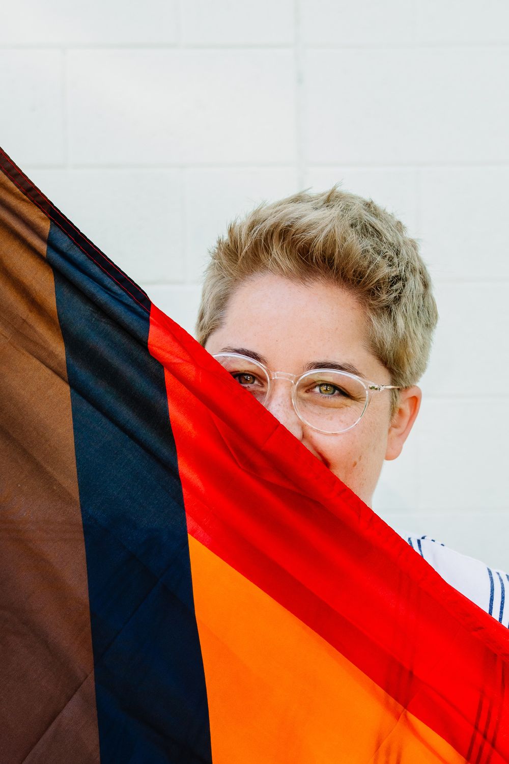Close-up shot of someone partially hidden behind a rainbow pride flag against white background.