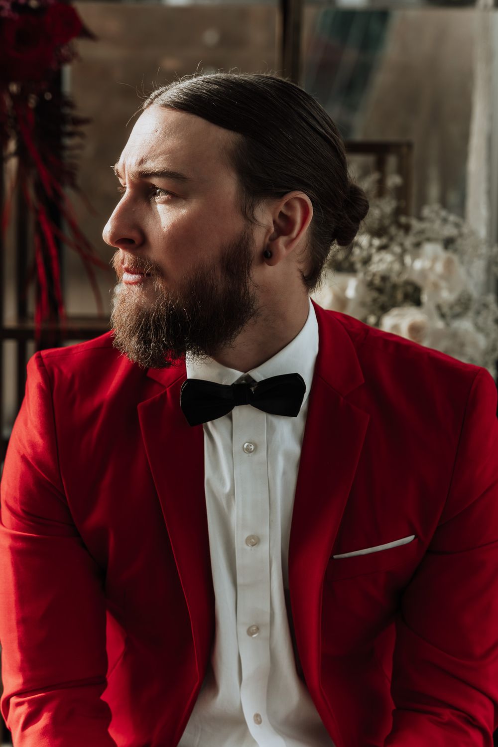 Profile shot of groom wearing red velvet jacket and black bowtie with styled beard.