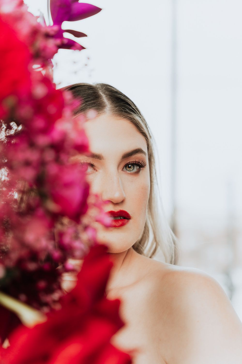 Dramatic bridal portrait with deep red flowers framing a stunning makeup look.