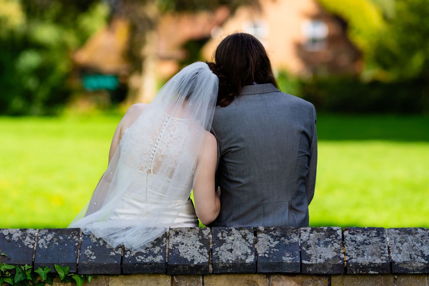 Newlywed couple sitting together on stone wall overlooking garden.