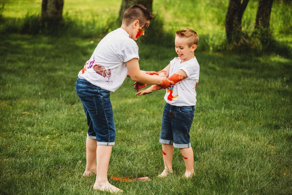 Children playing with colorful paint on their hands in a sunny green field.