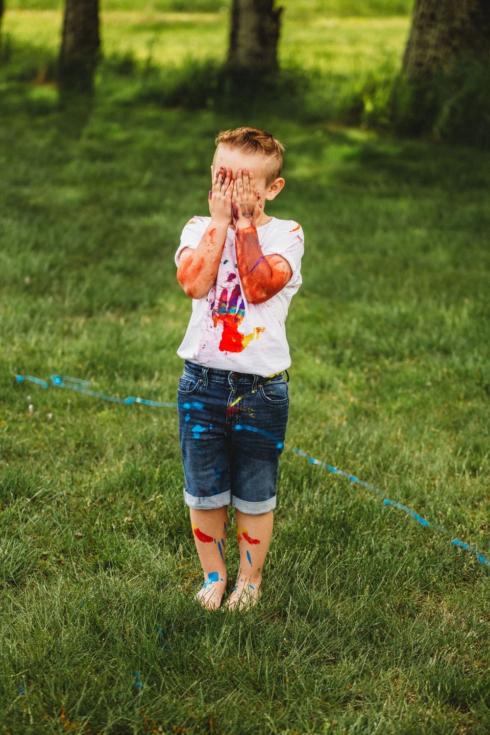 Child with messy paint hands playing outdoors in summer.
