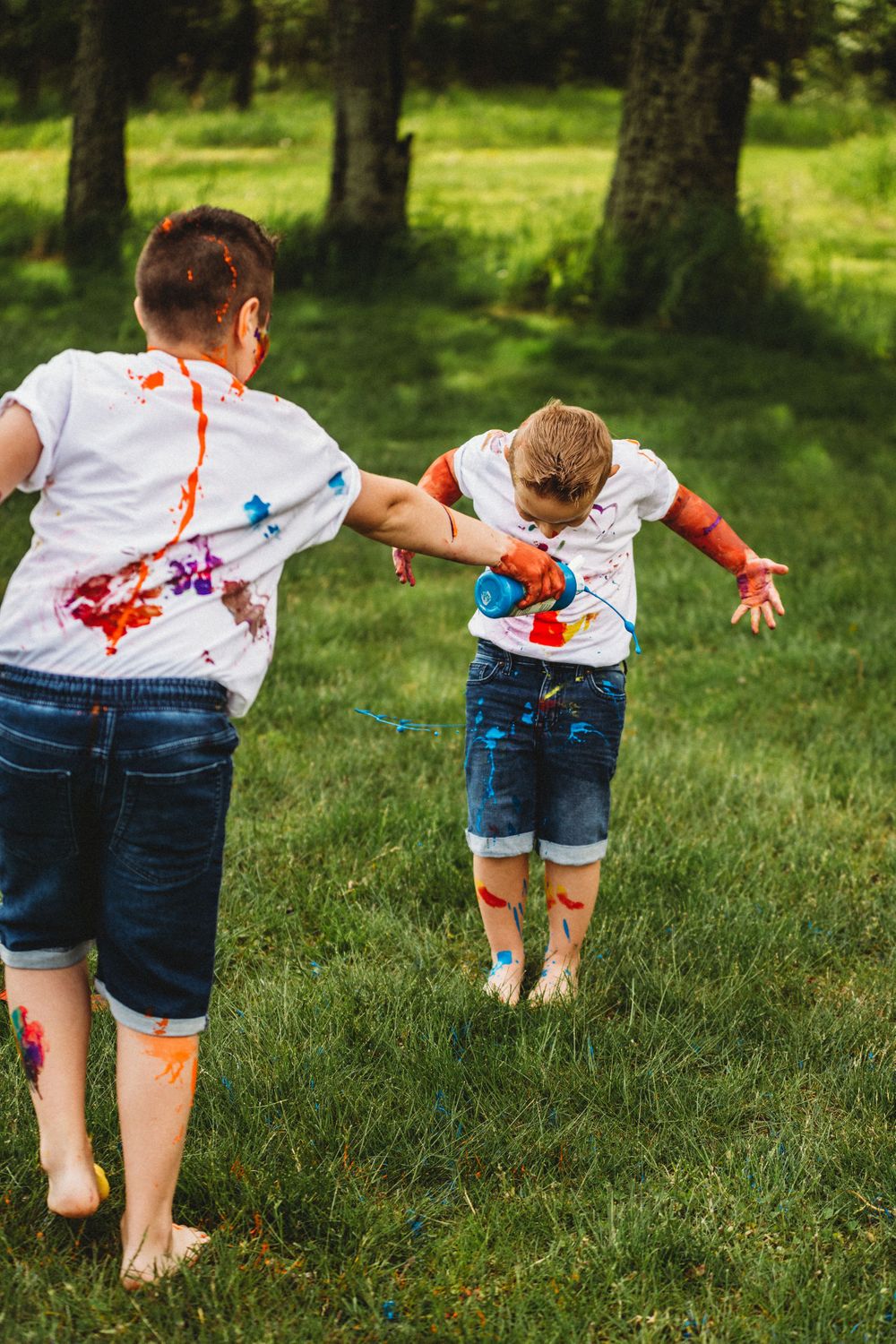 Kids running through grass with colorful paint-covered hands and shirts.