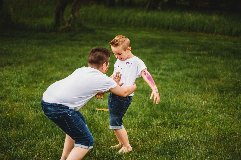 Active play with paint-covered hands and white shirts in a sunny garden setting.