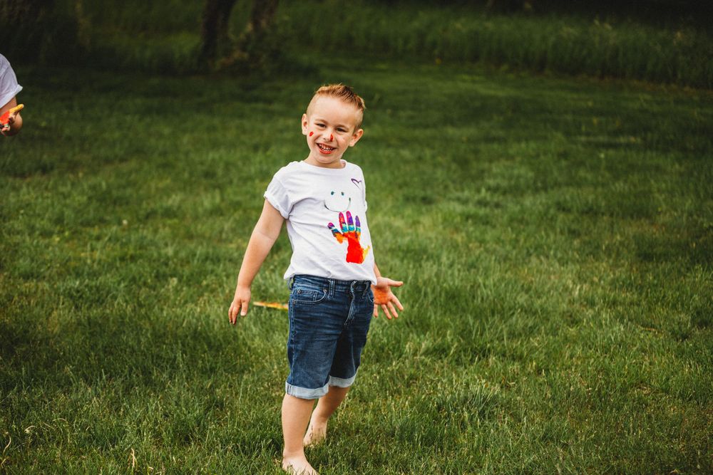 Playing with paint and making colorful handprints on white t-shirts in grassy field.