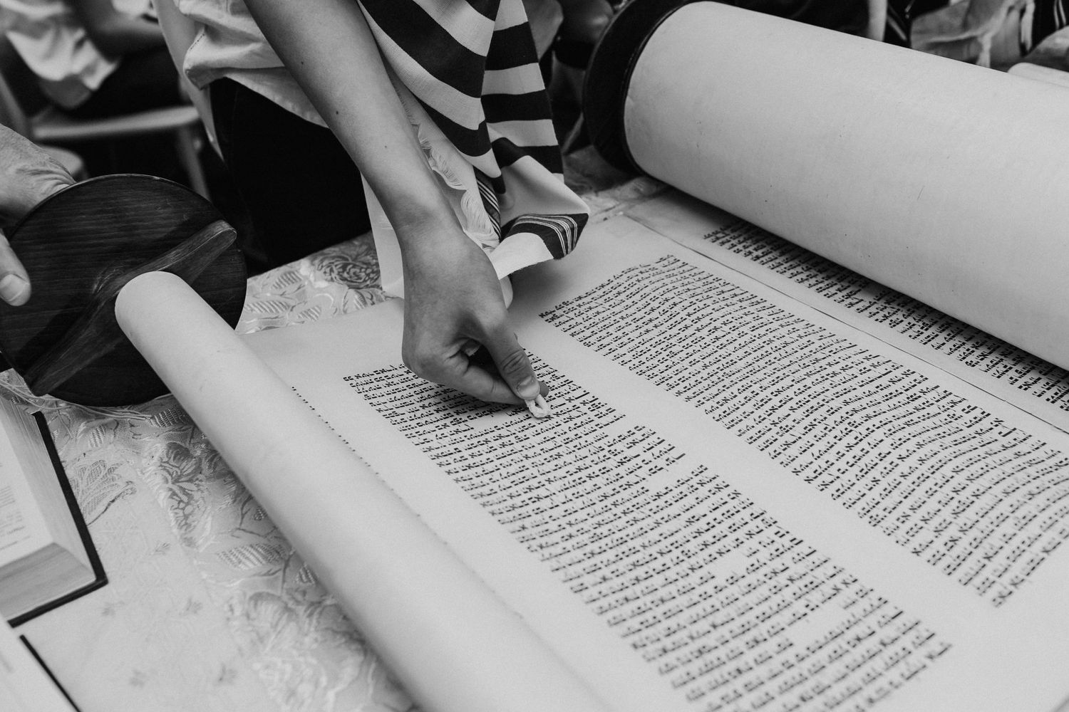 Child's hand pointing at Hebrew text in Torah scroll during Bar Mitzvah ceremony.