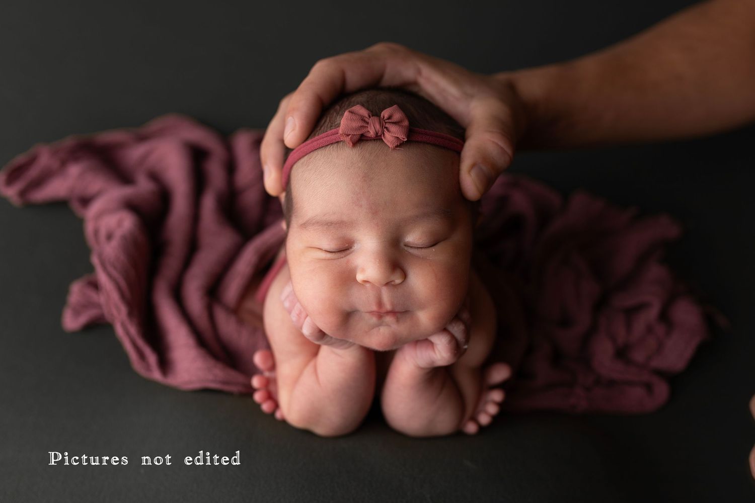 Sleeping newborn resting face on hands with burgundy fabric backdrop.