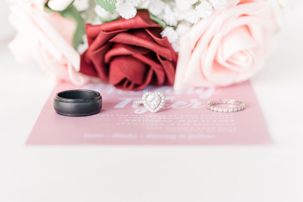 Wedding rings displayed with red and pink roses against soft background.