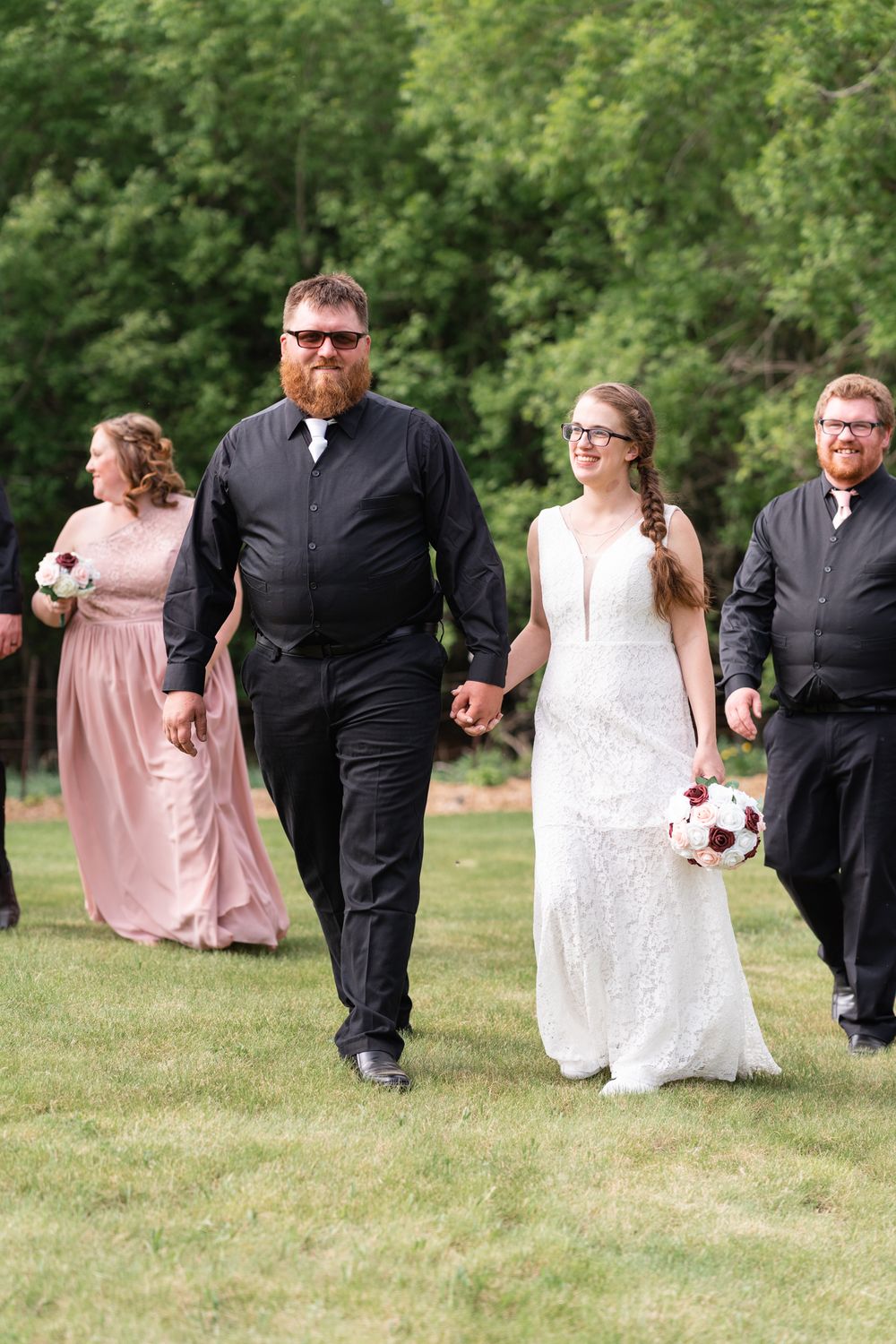 Wedding party walking together on green lawn with trees in background.