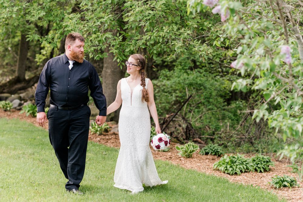 Newlyweds walking hand in hand through a garden pathway carrying a bouquet.