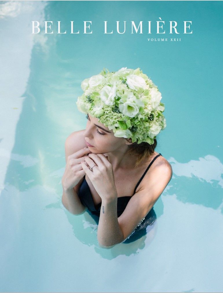 A woman swimming in an aqua blue pool while wearing a floral swim cap made with real flowers. Cover of Belle Lumiere Mag