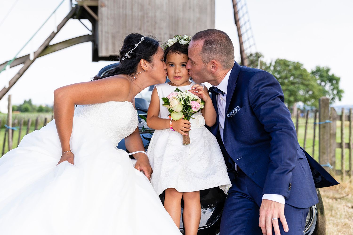 Joyful wedding portrait with couple and child sitting together outdoors.