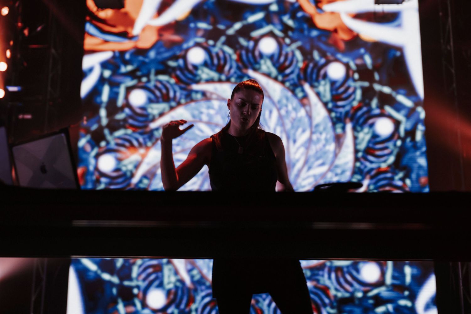 Concert performer silhouetted against vibrant blue spiral visuals on large display screen during live show.