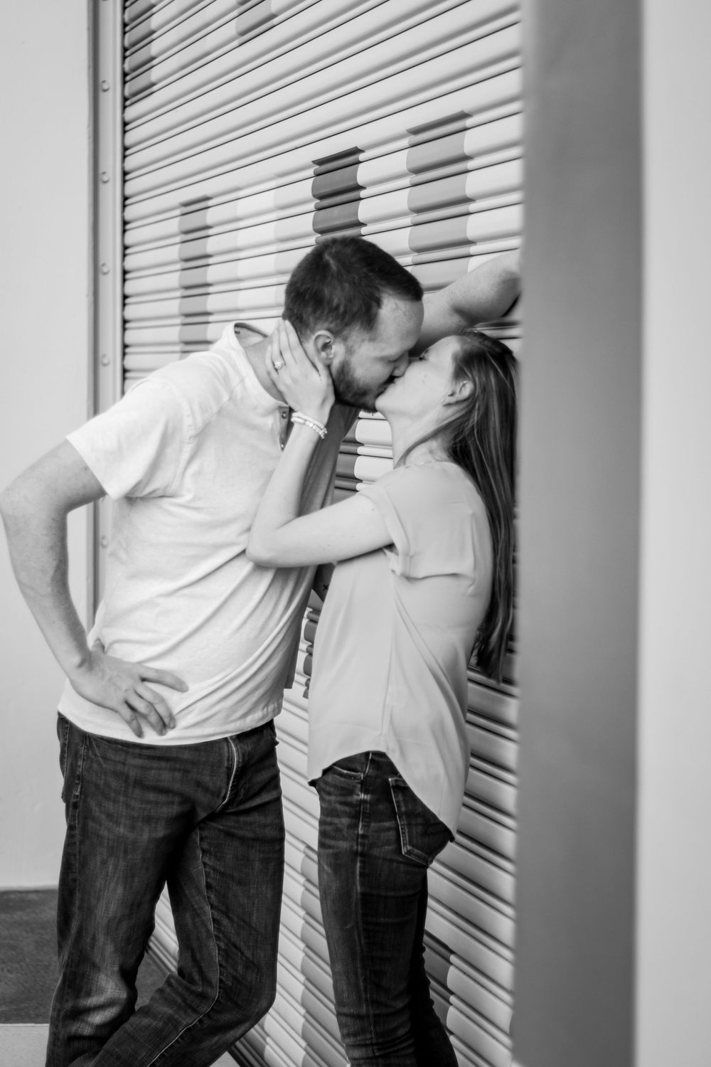 Romantic couple poses against industrial rolling door in black and white series.