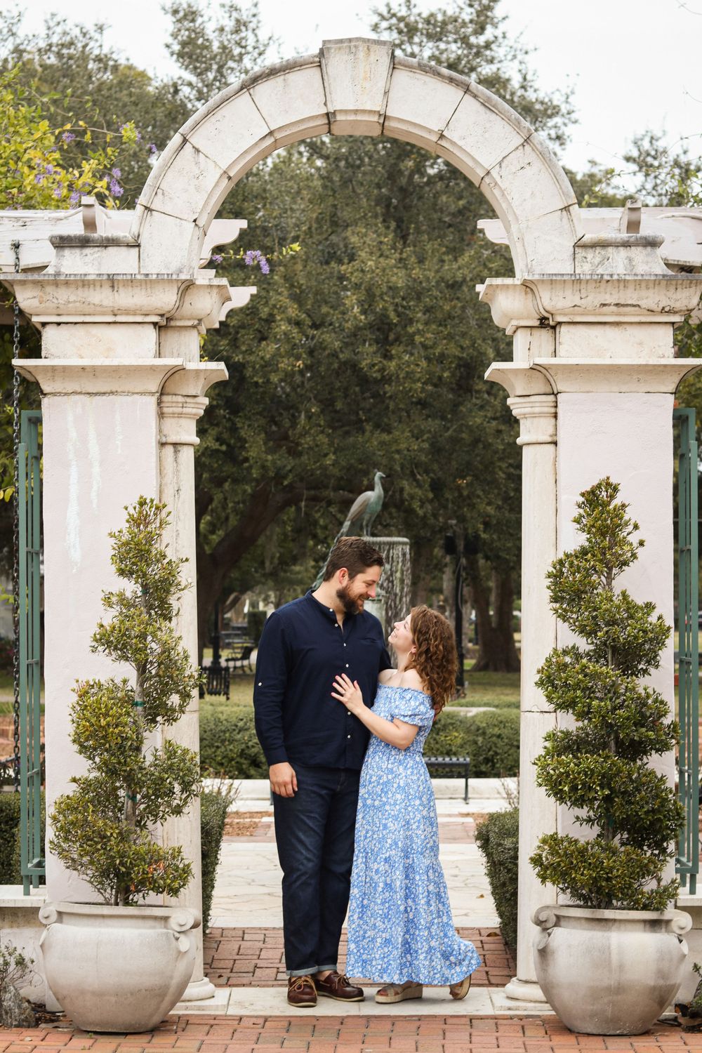 Romantic moment under white stone archway with potted plants and garden setting.
