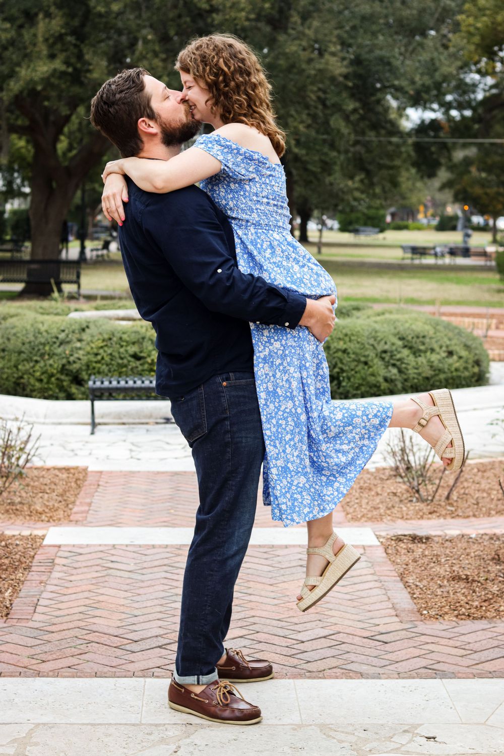 Couple in romantic embrace with blue floral dress and navy attire on brick path outdoors.