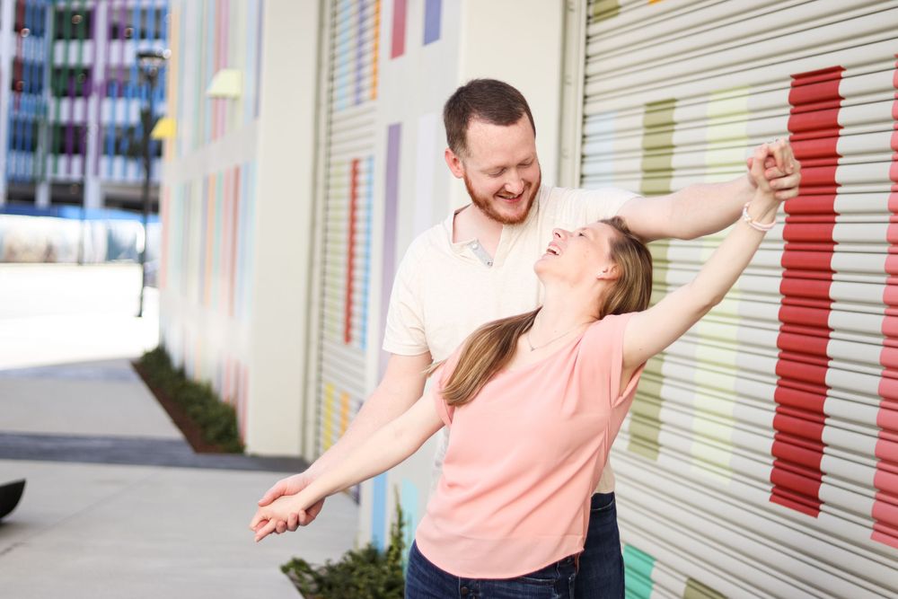 Dancing couple in casual attire photographed against colorful striped wall.