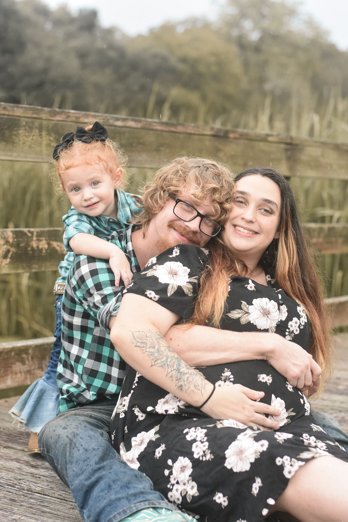 Candid family portrait on rustic wooden deck with natural greenery backdrop.