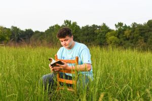 Person in blue shirt sits in tall grass field during summer.