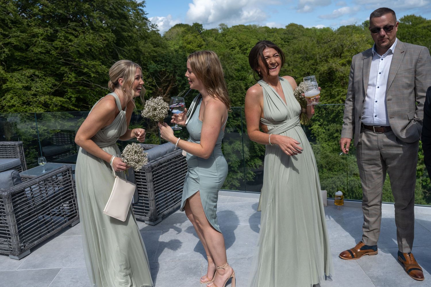 Wedding party members in sage dresses and formal attire gathered on an outdoor patio.