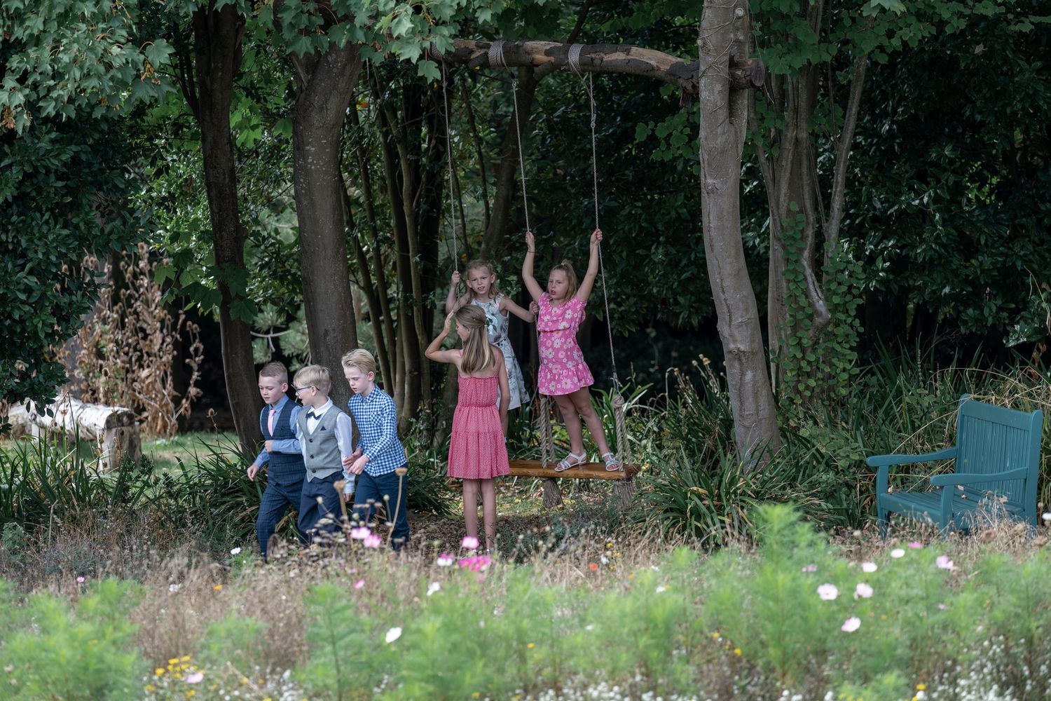 Children playing and jumping in a wooded garden area during a celebration.