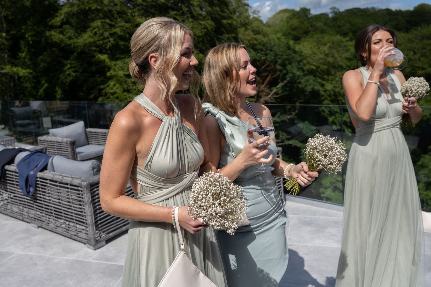 Bridesmaids in pale green dresses sharing a joyful moment on a terrace.