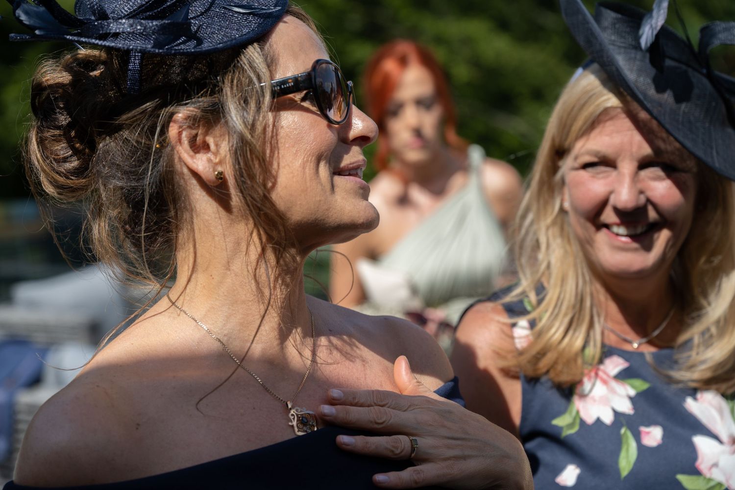 Wedding guests in elegant attire and fascinators enjoying an outdoor celebration.