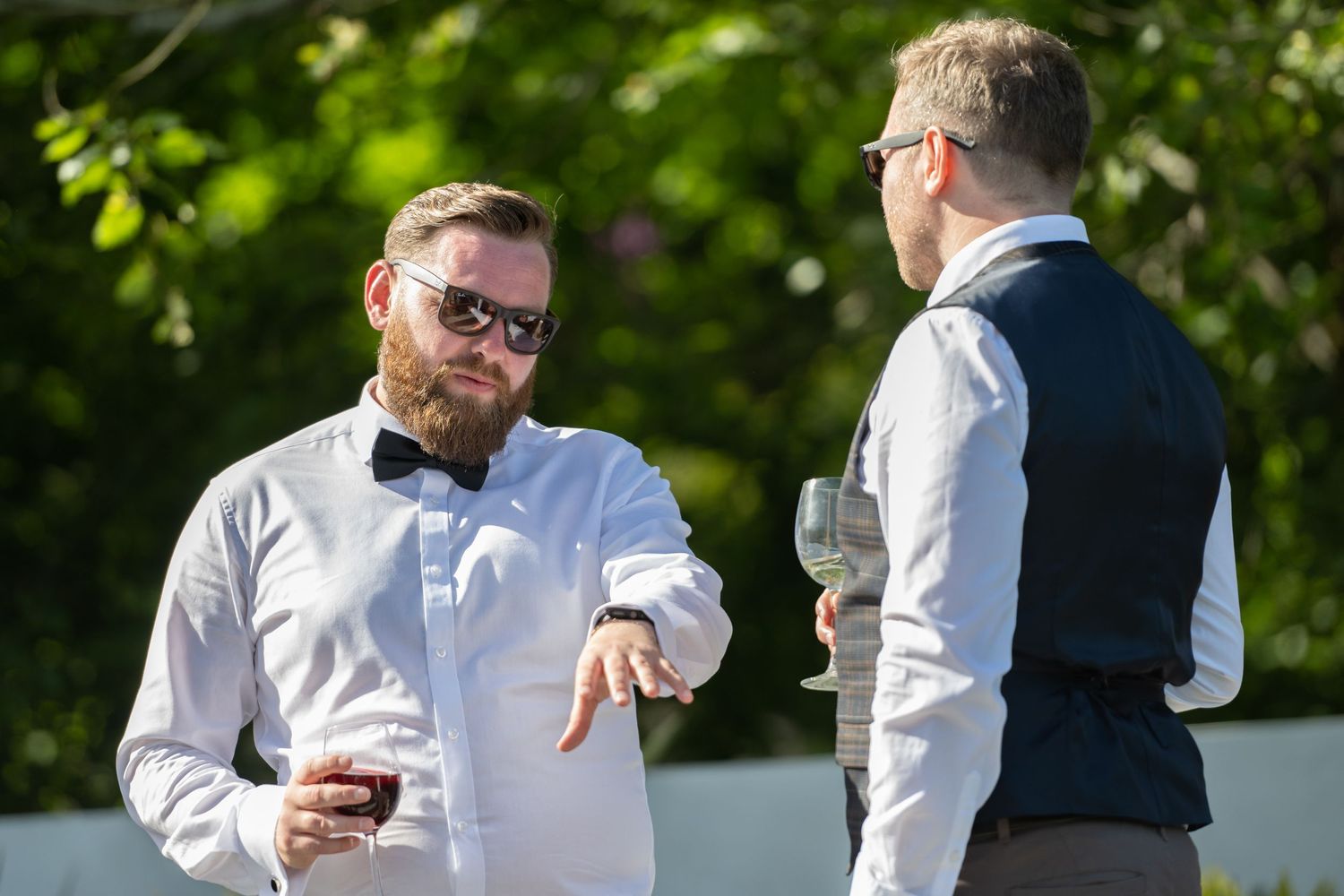 Two guests in formal attire having conversation during outdoor wedding reception.