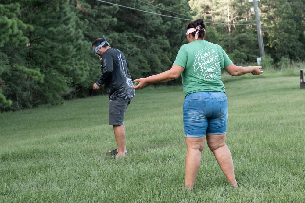 Two people playing a game on a grassy hillside near a forest.